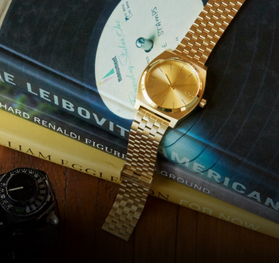 Gold Nixon Time Teller watch sitting across stack of books.